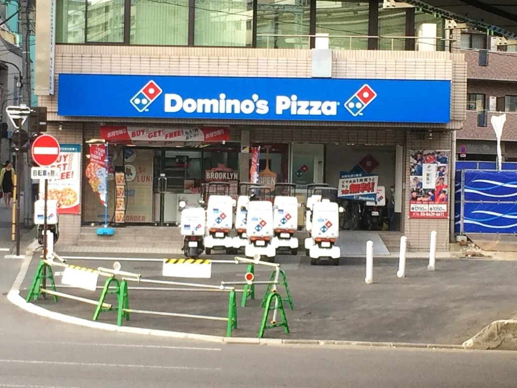 東京都内のドミノ・ピザ店舗に並ぶ配達車両の写真
